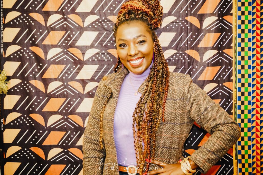 A woman with long braids standing in front of a wall.